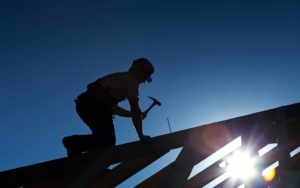 Roofer hammering in a large nail into the frame of a house