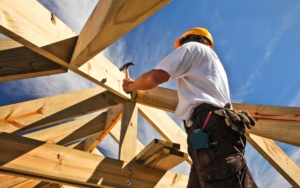 Roofer hammering nail into the frame of a house