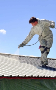 Roofing worker spraying a material on a metal roof vertical