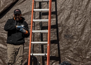 Roofer standing in front of tarp next to an orange ladder