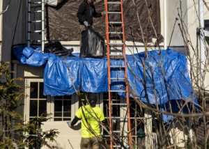 Two roofers removing debris from a roof covered in tarps