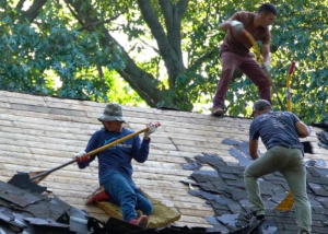Three roofers tearing shingles of roof with shovels
