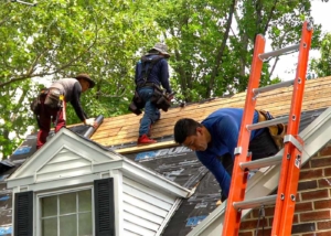 Three roofers fixing a roof, orange ladder in front