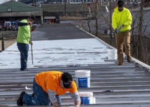 Three roofers repainting a commercial roof