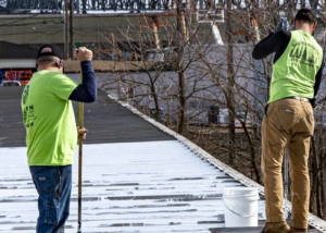Two roofers repainting a commercial roof