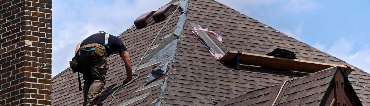 Man climbing up roof wearing tool belt fixing broken shingles. chimney to the left and dormer below him