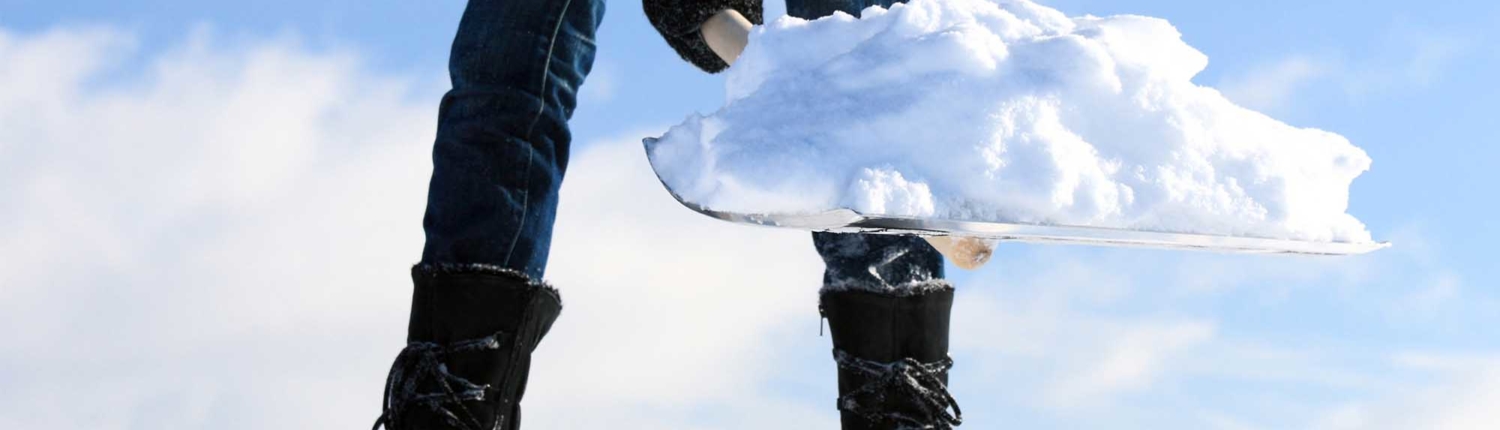 Close up of a shovel holding a pile of snow with person holding shovel wearing black boots and gloves