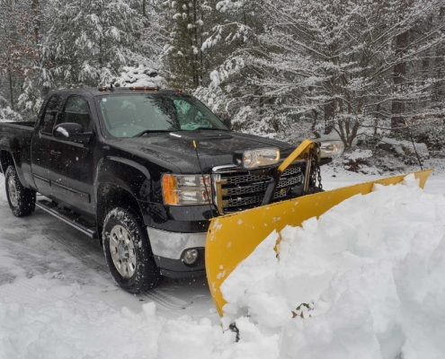 Black truck plowing snow in a wooded area