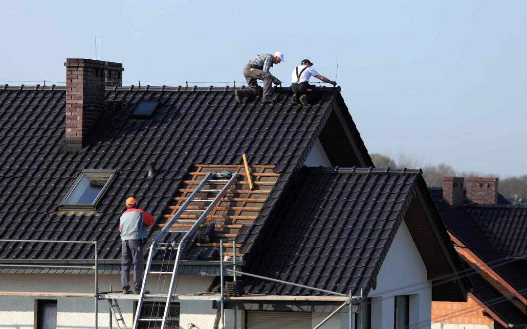 Team of roofers working on top of a black shingled roof and a brick chimney, sky in background