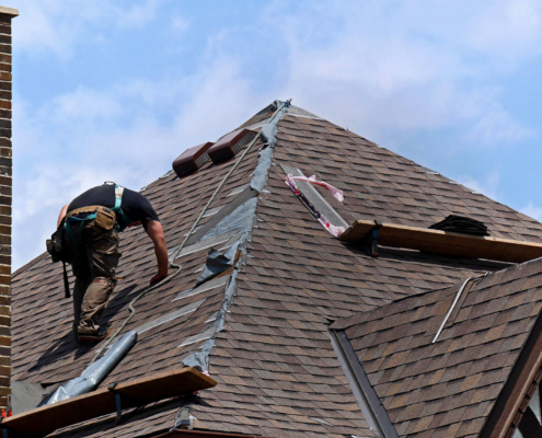 Roofer repairing shingle damage with chimney to the left