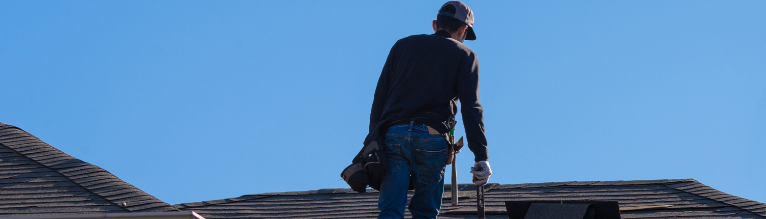Man walking up a residential roof holding tools, back to camera