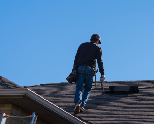 Man walking up a residential roof holding tools, back to camera