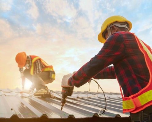 Two men in protective gear drilling into a commercial roof with the sky in the background