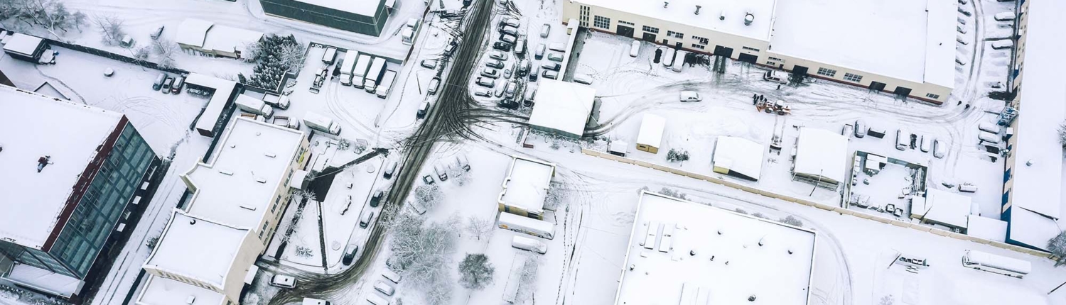 Birds eye view of a snowy office park with lots of cars covered in snow