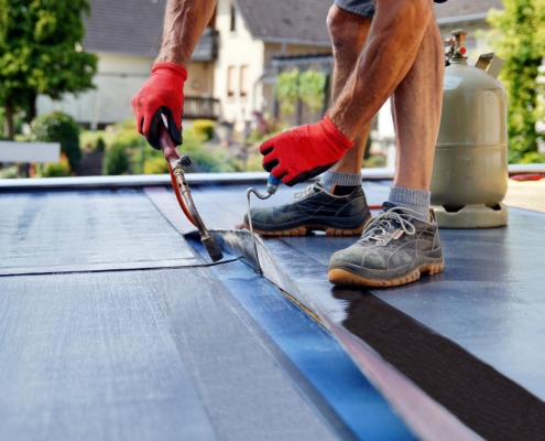 Image of a worker installing waterproof membrane on flat roof.